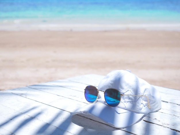 Blauwe zonnebril en hoed op witte tafel over zomer strand achtergrond
