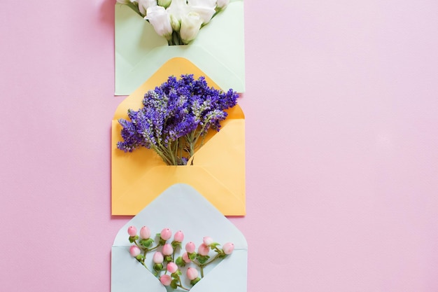 Blauwgele en groene enveloppen met bloemen erin op een roze achtergrond