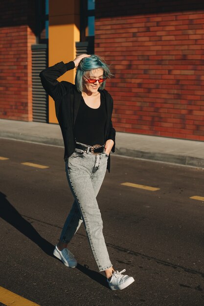 Blauwharige vrouw met bril loopt op straat terwijl ze tegen de zon poseren