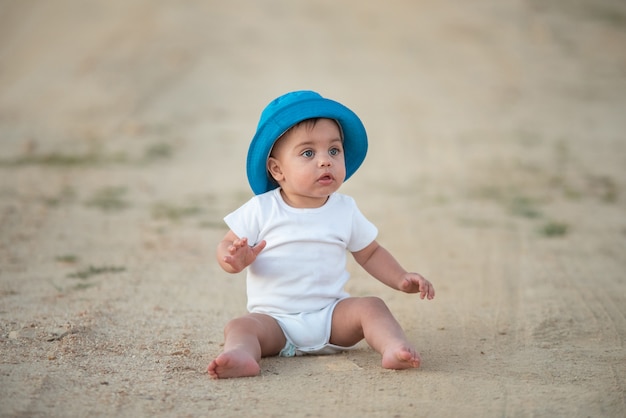 Blauwogige baby met blauwe hoedenzitting op de zandvloer