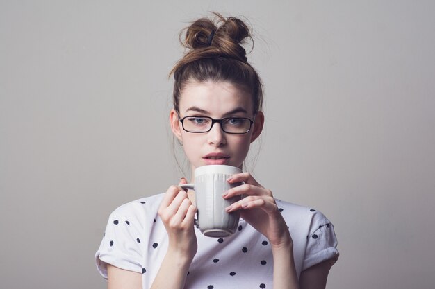 Foto blauwogige jonge vrouw in oogglazen, die wit polka dotoverhemd draagt, een koffie houdt