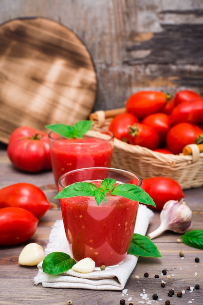 Смешанный свежий томатный сок с листьями базилика в очках на салфетке на деревянном столе