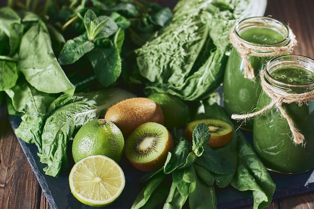 Blended green smoothie with ingredients on the stone board, wooden table selective focus