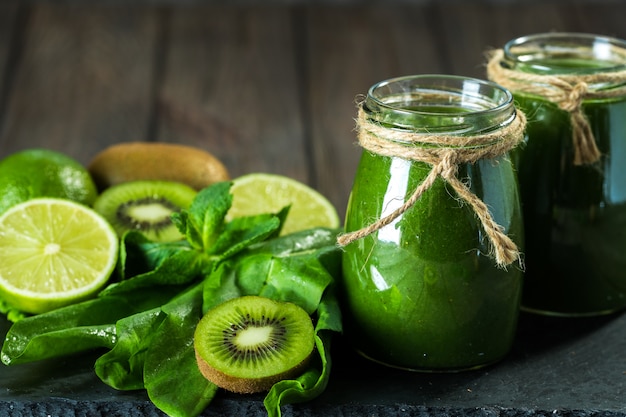 Blended green smoothie with ingredients on the stone board, wooden table