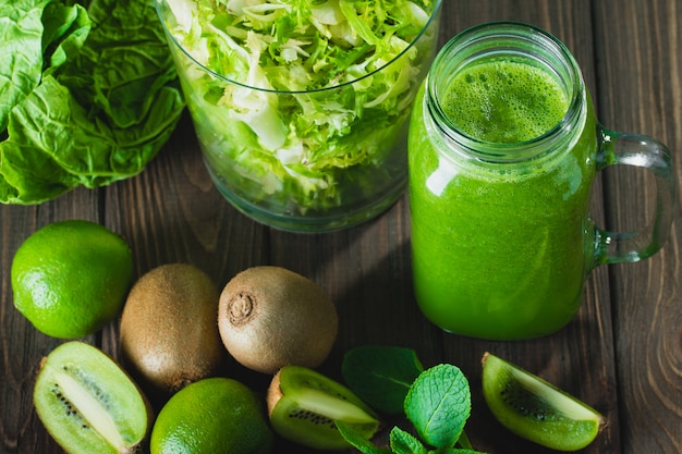 Blended green smoothie with ingredients on wooden table