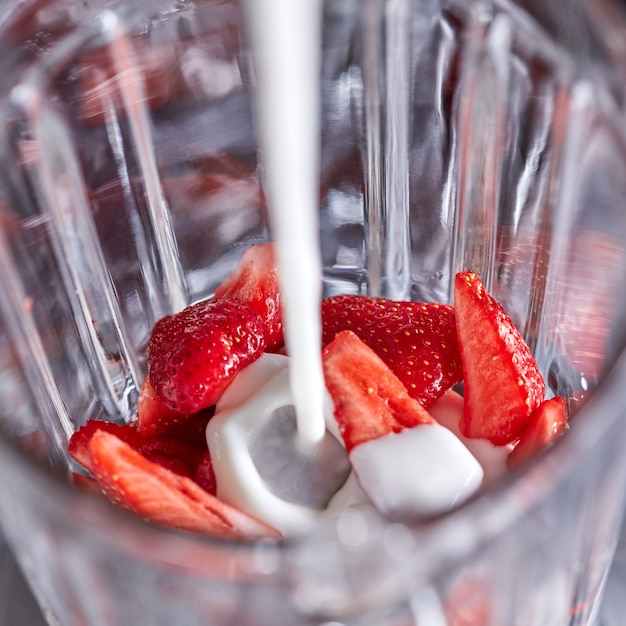 Un frullatore con pezzi di fragola viene versato con latte fresco preparazione passo passo della bevanda al latte top