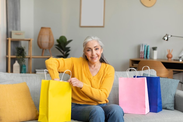 Blij blij mooie blanke senior vrouw shopaholic pakt tassen uit met aankopen zit op de bank