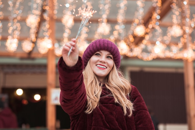 Blij blond meisje gekleed in stijlvolle kleding, met gloeiende sterretjes op de kerstmarkt in Kiev