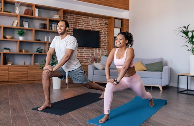 Blij dat jonge Afro-Amerikaanse koppelatleten in sportkleding oefeningen doen of yoga beoefenen