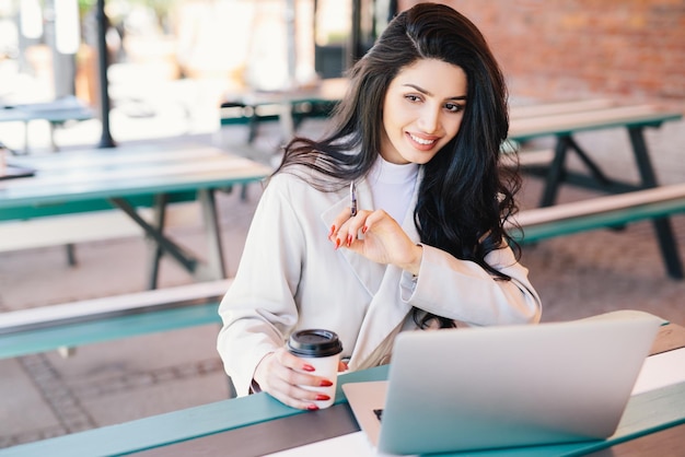 Blij dat jonge zelfstandige brunette vrouw geniet van gratis draadloze internetverbinding zittend voor generieke laptop op terras met afhaalmaaltijden koffie Ontspanning schoonheid en jeugdconcept