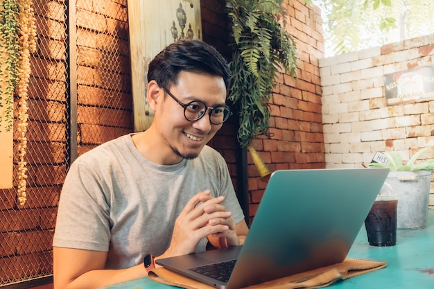 Blij en glimlach gezicht van man werkt op zijn laptop in het café.