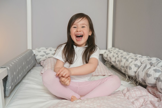 Blij kind dat zich klaarmaakt voor bed. De baby zit op het bed en verheugt zich