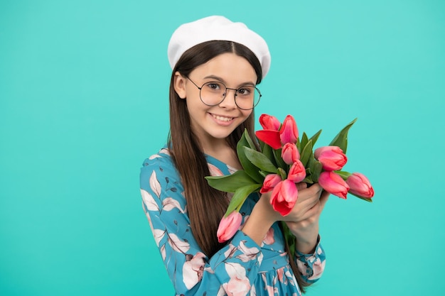 Blij kind in baret met tulpen moeders of womens dag kind in glazen houden bloemen voor 8 maart tiener meisje met lente boeket op blauwe achtergrond bloemen aanwezig