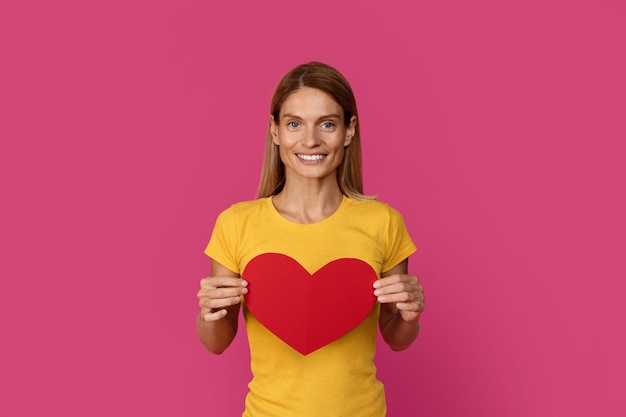 Blij lachende mooie Europese blonde vrouw van middelbare leeftijd met een groot hart geniet van het liefdesgevoel