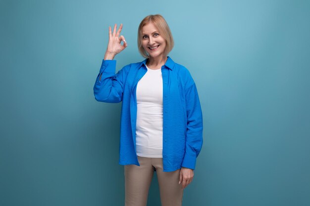 Blij lachende vrouw van middelbare leeftijd in een blauw shirt op een blauwe achtergrond met kopieerruimte