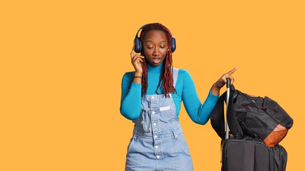 Blij meisje dat naar muziek luistert, danst en een audiokoptelefoon gebruikt, met een trolley en reistassen in de studio. Lachende vrouw doet dansbewegingen en geniet van mp3-nummers op koptelefoon.