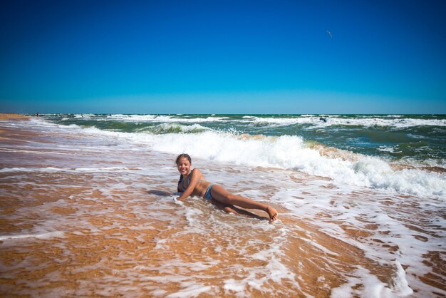 Blij mooi meisje geniet van warm zeewater aan de zandige kust op een zonnige warme zomerdag. Vakantie- en ontspanningsconcept met kinderen