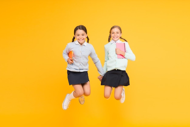 Blij om terug naar school te zijn basisschoolleerlingen in de lucht kleine meisjes springen met boeken op gele achtergrond kleine kinderen genieten van schoolpauze verwelkom de kinderen op school