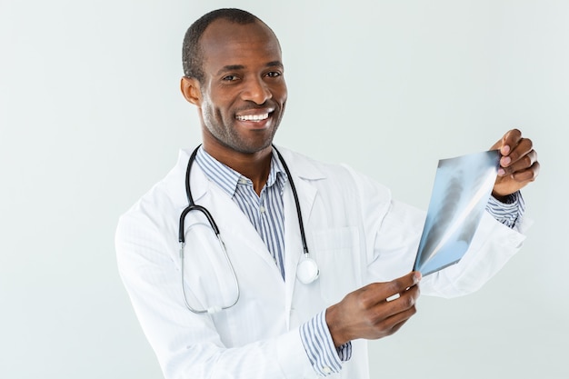 Blij professiaonl afro-amerikaanse arts die röntgenscan houdt terwijl hij bij het werk betrokken is