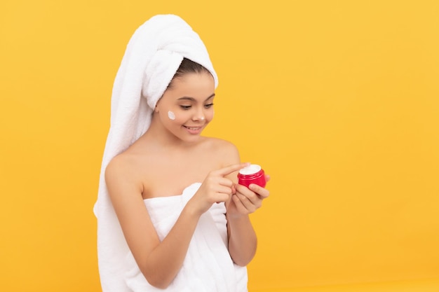 Blij tienermeisje in douchehanddoek gezichtscrème aan te brengen