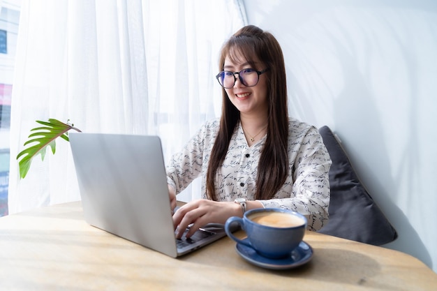 Blij van aziatische freelance mensen zakelijke vrouwelijke casual werken met laptopcomputer met koffiekopje en smartphone in coffeeshop communicatieconcept