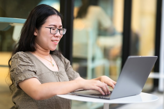 Blij van aziatische freelance mensen zakelijke vrouwelijke casual werken met laptopcomputer met koffiekopje en smartphone in coffeeshop zoals de achtergrond, communicatieconcept