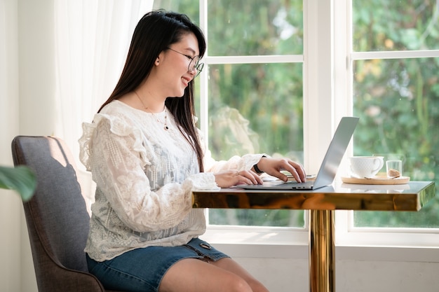 Blij van aziatische freelance mensen zakelijke vrouwelijke casual werken met laptopcomputer met koffiekopje en smartphone in coffeeshop zoals de achtergrond, communicatieconcept