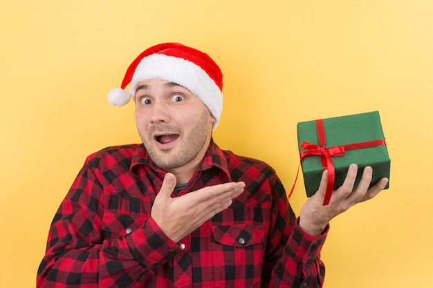 Blij verrast man in een rode hoed met een geschenk met bewondering op zijn gezicht