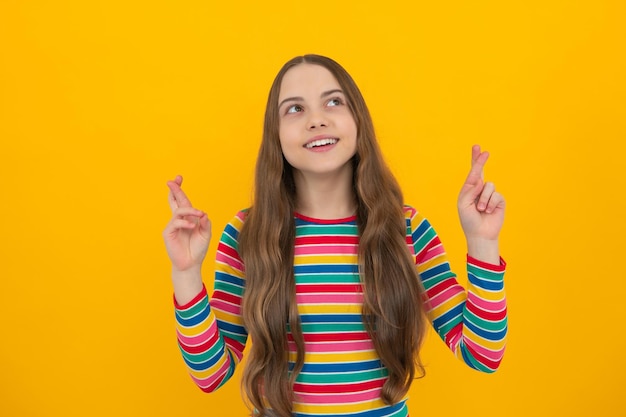 Blij, vrolijk tienerkind dat geluk wenst, kruist vingers heeft vertrouwen voor beter geïsoleerd over gele achtergrond