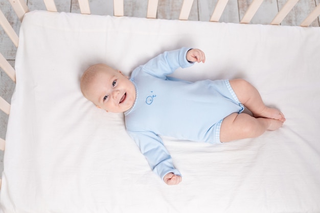 Blije baby ligt in de wieg, schattige kleine jongen van zes maanden ligt in de kinderkamer op het bed