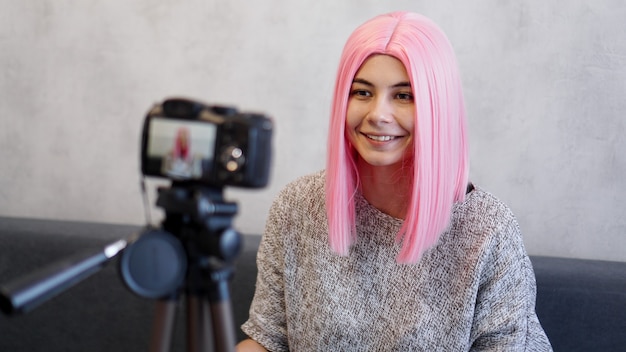 Blije blogger in roze pruik voor de camera op een statief. Ze neemt een video op