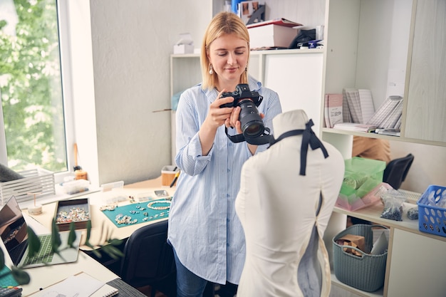 Blije blonde vrouw die haar camera op etalagepop richt terwijl ze professionele foto's maakt