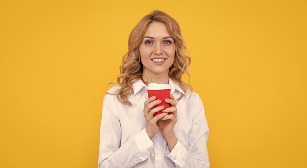 Blije blonde vrouw met een kopje koffie in de ochtend op gele achtergrond