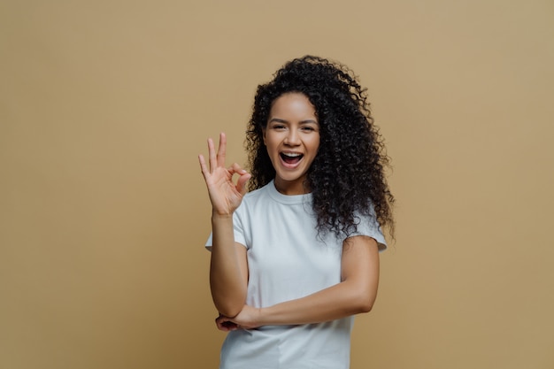 Blije gekrulde jonge vrouw maakt goed gebaar