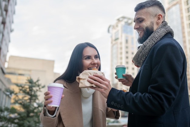 Blije gelukkige man die een boterham houdt terwijl hij zijn geliefde vrouw beloont