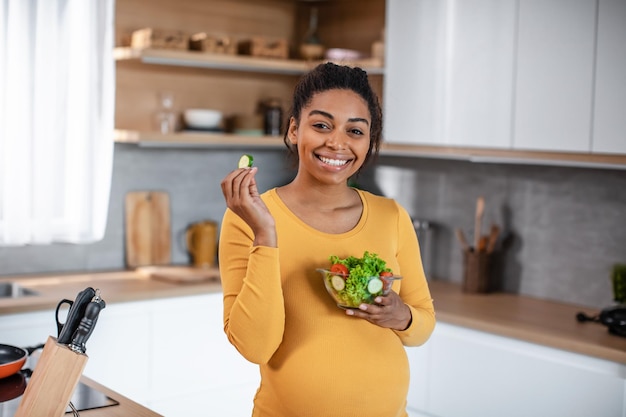 Blije hongerige mooie duizendjarige zwangere Afro-Amerikaanse vrouw met buik die salade van groenten eet