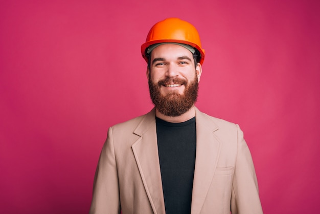 Blije jonge architectenmens die zich over roze backgorund bevindt en de camera bekijkt