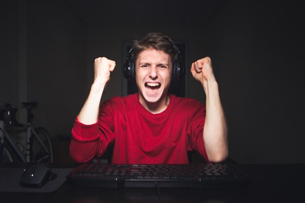 Blije jonge mens met hoofdtelefoons die thuis een computerspel spelen