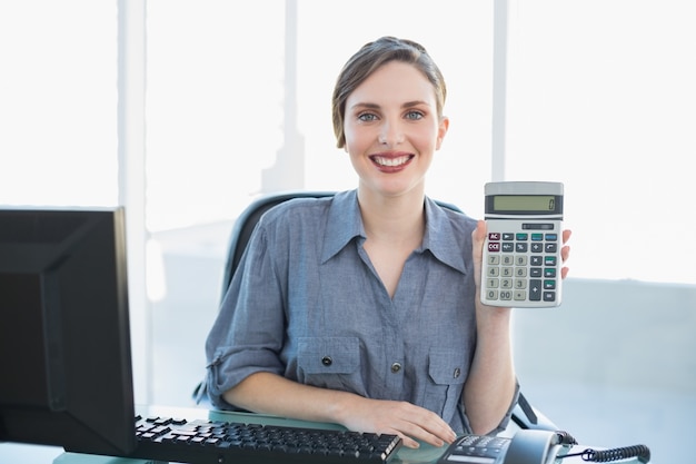 Blije jonge onderneemster die calculatorzitting bij haar bureau toont