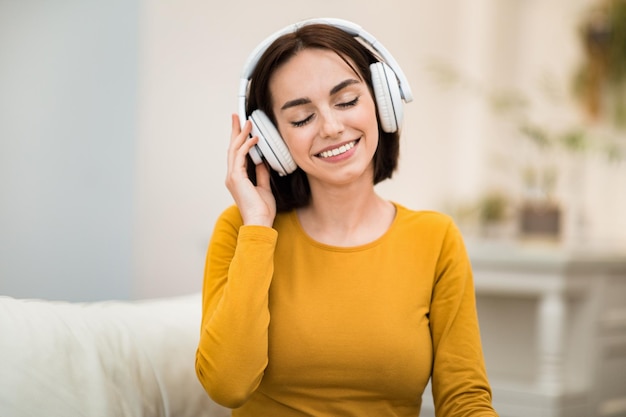 Blije jonge vrouw die naar muziek luistert met behulp van draadloze hoofdtelefoons