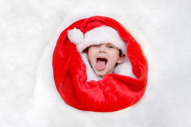Blije jongen in de hoed van de Kerstman stak zijn tong uit