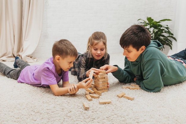 Blije kinderen zitten op de grond en spelen een educatief spel (jenga) en staan in een toren van blokken