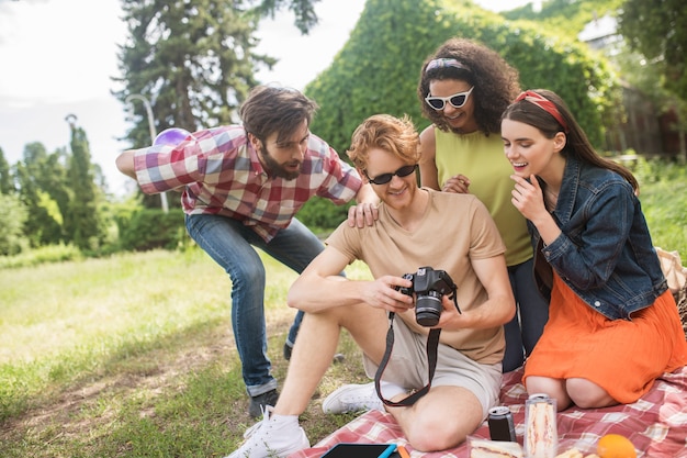 Blije mensen. Jonge gelukkige vrienden kijken naar foto op camera met rust op picknick in het park op mooie dag