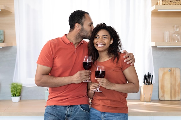 Blije millennial zwarte man met glas rode wijn kussen vrouwelijke knuffels wensen gelukkige verjaardag geniet van vrije tijd
