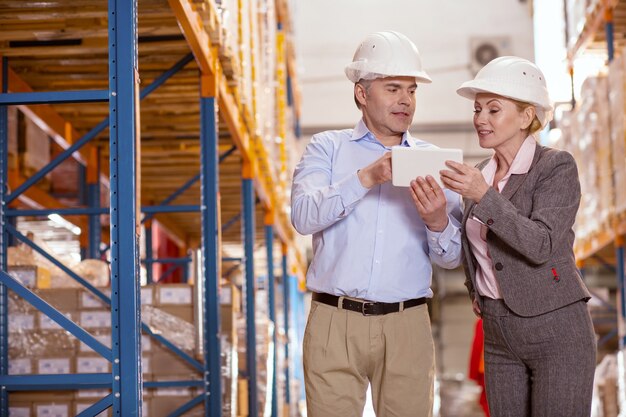 Blije positieve mensen die naar het tabletscherm kijken terwijl ze als managers in het magazijn werken