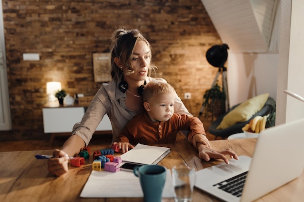 Blijf thuis moeder werkt op laptop terwijl ze op haar zoontje past