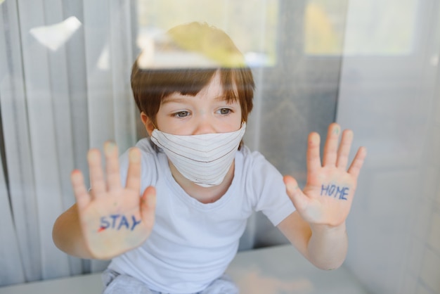 Blijf thuis quarantaine coronavirus pandemie preventie. verdrietig kind zowel in beschermende medische maskers in de buurt van ramen en kijkt uit raam