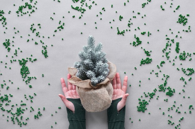 Blijf zo lang mogelijk je nep-kerstboom gebruiken. Alternatieve groene eco vriendelijke kerst concept. Handen tonen plastic boom verpakt in jute met plastic verspreid over ambachtelijk papier.