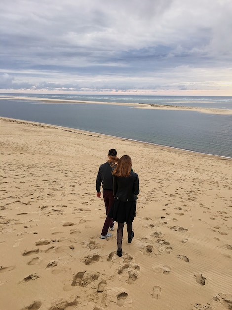 Blijft de schoonheids jonge vrouw in jasje man hand houden en naar het strand op de herfstdag van de kust dalen