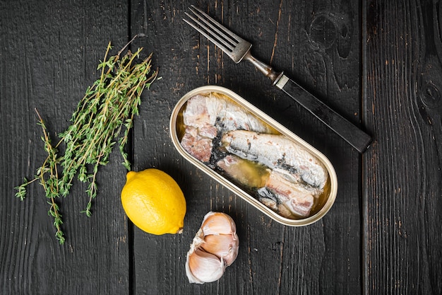 Blikje zeevruchten sardines vis set, op zwarte houten tafel achtergrond, bovenaanzicht plat lag